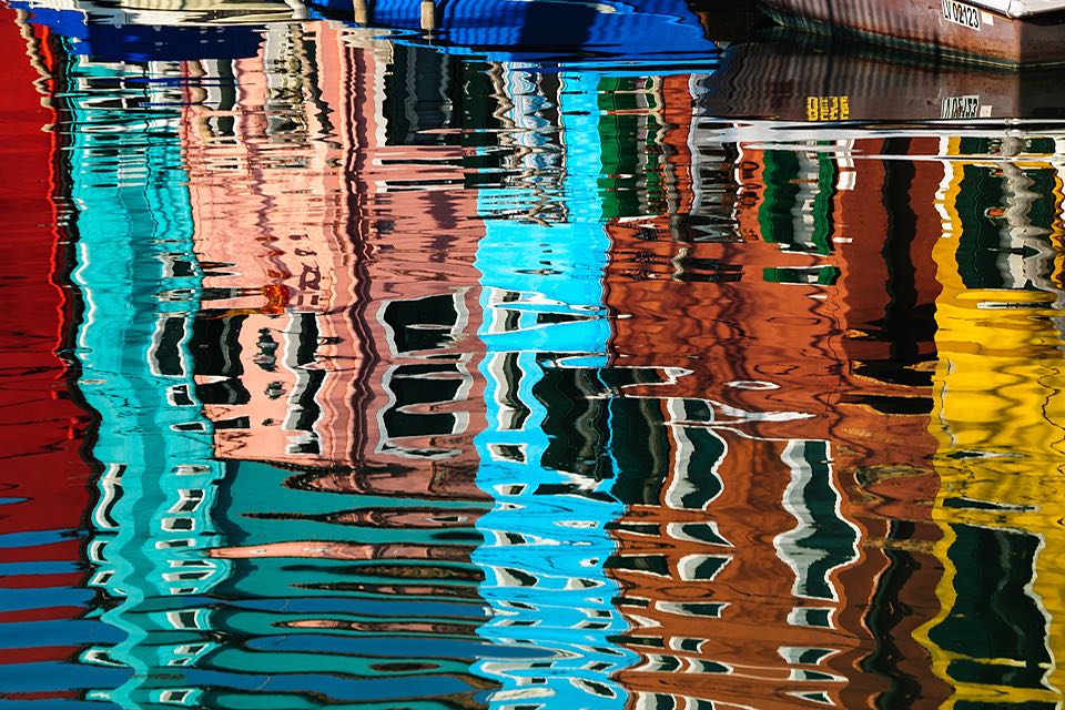 Wasserspiegelungen der bunten Haeuser auf Burano Venedig